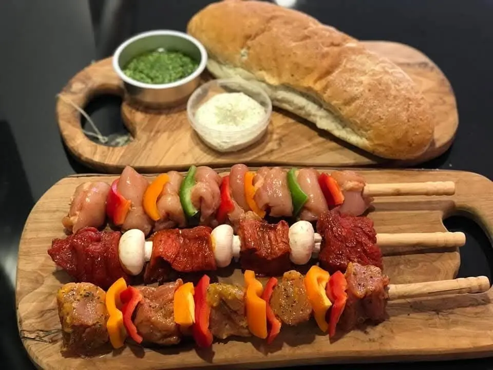 BBQ-spiezen op een plank met stokbrood, kruidenboter en tapenade