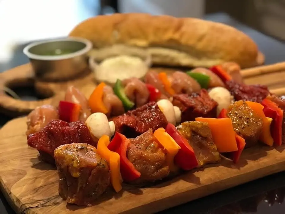 Gemarineerde vleesspiesen met paprika op een houten plank naast stokbrood